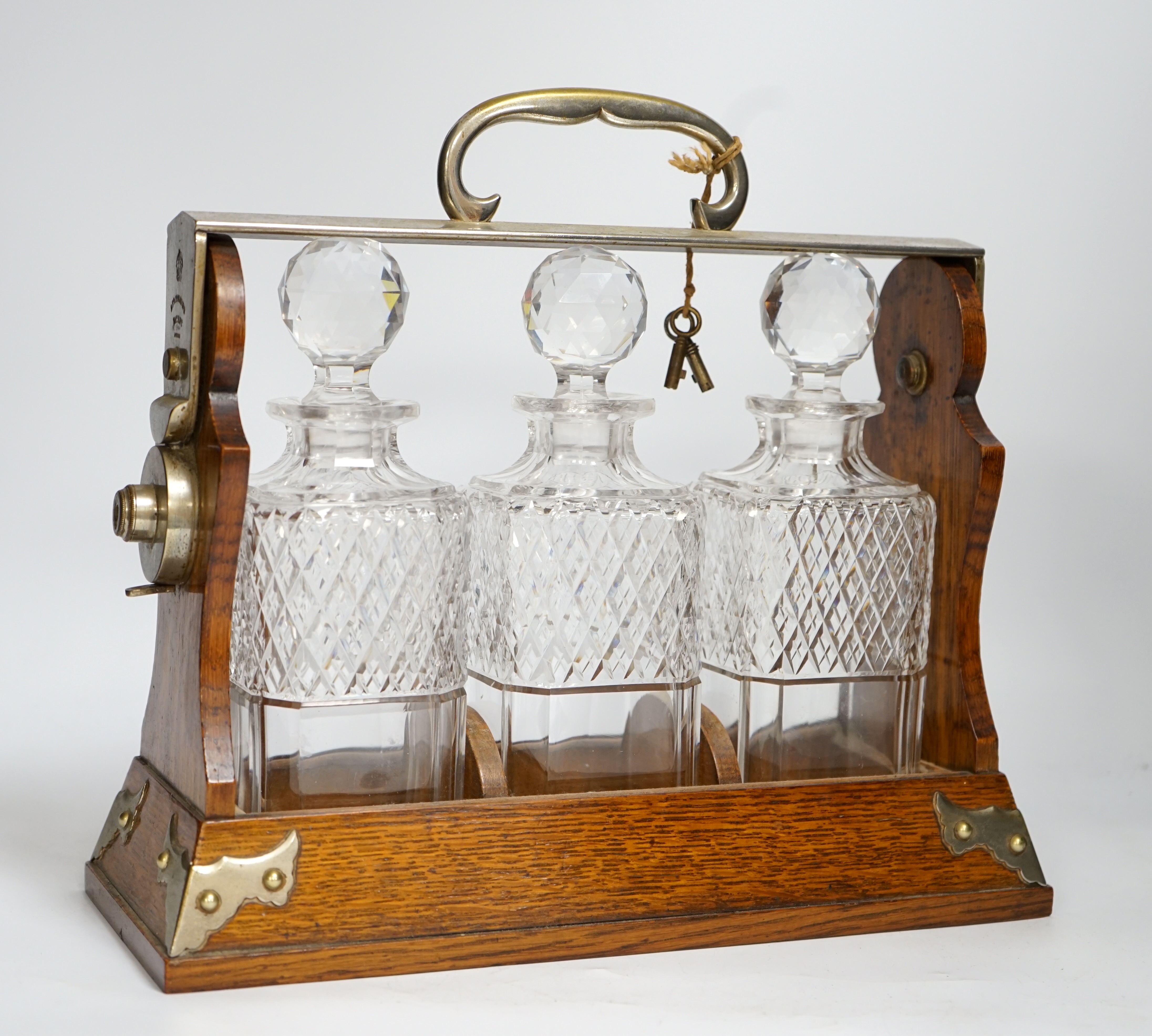 A Betjemann’s patent oak three bottle tantalus with key, 32cm wide